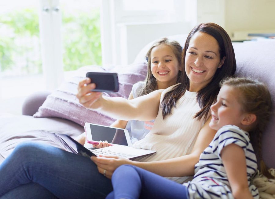 Mother and daughters taking selfie on living room sofa